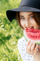 Beautiful woman is biting slice of watermelon on green grass background.