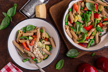 whole grain penne pasta with grilled vegetables ( zucchini, peas, bell pepper ant tomato) and cheese on pan