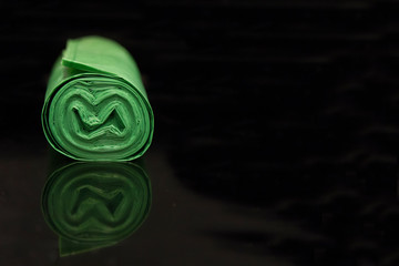 green garbage bag rolled up on a black background with reflection