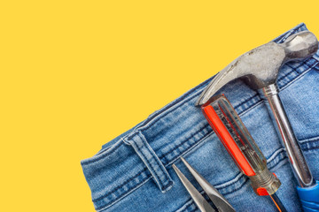 Jeans, screwdriver, hammer and pliers on yellow background. Jeans texture, Blue denim jeans with...