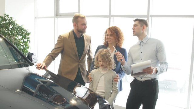 Affable caucasian consultant and customer in dealership. People came to get new automobile, open-minded salesman help to choose and make decision, buy new auto.