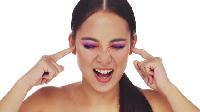 A irritated young half-naked woman with bright fashion eye makeup is covering her ears with her fingers isolated over white background. Showing nonsense content