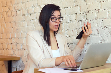 A young beautiful girl is broadcasting live in a trendy cafe and is holding a phone in her hands.