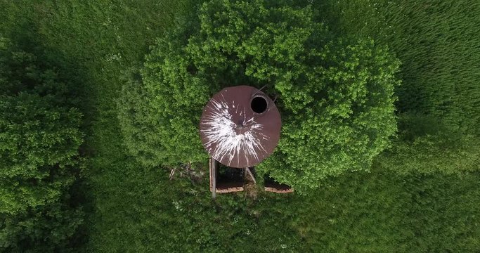 4K aerial summer morning high quality video footage of old unused rusty metal water pressure tower among lush green vegetation in European landscape