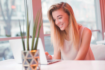 elegant young positive beautiful girl,using laptop computer in a cafe,successful happy business woman,working,looking for information,browsing internet, smiling and looking at you,blurred background