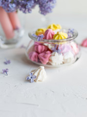 Some meringue kisses in a glass jar on the wait background decorated with bouquet of fresh lilac flowers. Spring season.