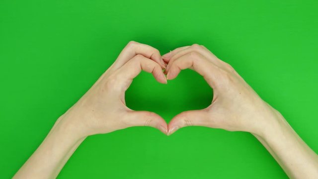Female hands show a symbolic heart on a green screen background. Movement from bottom to top, chromakey