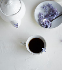 Breakfast with black tea or coffee and meringue kisses on the white table. Spring lilac flowers in a glass vase.