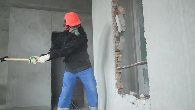 demolition work and rearrangement. worker with sledgehammer at wall destroying