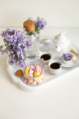 Breakfast with black tea or coffee and meringue kisses on the white table. Spring lilac flowers in a glass vase.