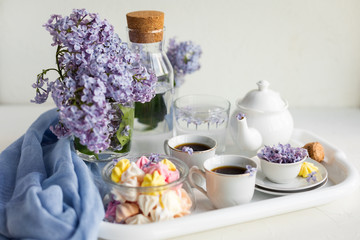 Breakfast with black tea or coffee and meringue kisses on the white table. Spring lilac flowers in a glass vase.