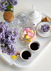 Breakfast with black tea or coffee and meringue kisses on the white table. Spring lilac flowers in a glass vase.