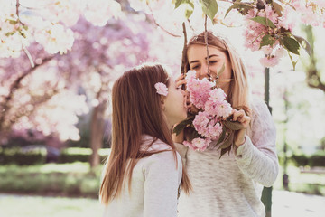 Sakura blossomed. Young mother with her child have fun in the park near the sakura. Spring morning. They look at each other