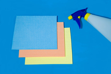 Hand-held household spray for cleaning liquids and three rectangular multi-colored napkins on a blue background. The concept of cleanliness in the house, wet cleaning. Household. Selective focus