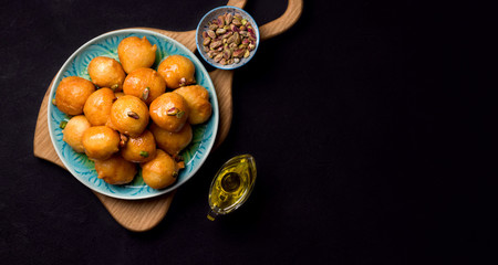 Lokma is a sweet dish in Greek, Turkish, Persian and Arabic cuisines. Dessert of sweet fried balls in a plate on a black background