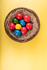 Wicker basket of colorful Easter eggs isolated on yellow