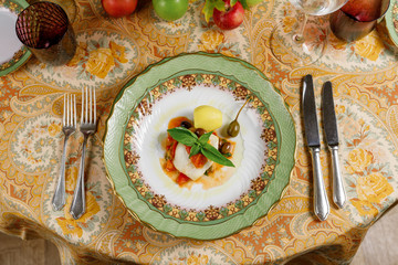 white fish with potatoes, basil and olive with sauce on a plate  and on a table. top view on a tablecloth