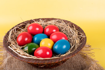 Wicker basket of colorful Easter eggs isolated on yellow