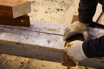 Painting a wooden element with brown paint. Hands in working gloves hold a wooden product and a brush.