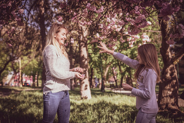 Fototapeta premium Sakura blossomed. Young mother with her child have fun in the park near the sakura. Spring morning. They look at each other