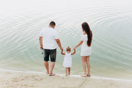 Mom, dad hugging daughter walking on the beach near lake. The concept of summer holiday. Mother's, father's, baby's day. Family spending time together on nature. Family look
