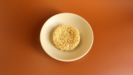 Raw dry instant noodles in a deep ceramic beige soup bowl on a brown background. pasta, for the preparation of which it is enough to pour boiling water and wait a few minutes. Copy space.