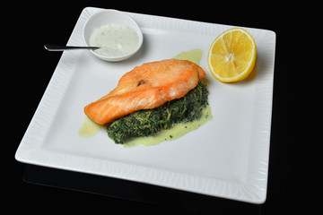 Salmon steak with spinach and lemon sauce on a white plate