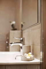 White ceramic washbasin, glossy metal faucet and a delicate white flower lying on the edge of the washbasin