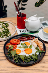 Fried eggs with fried eggs, sausage, tomatoes, Basil on a black plate