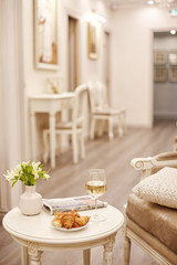 A glass of white wine, crispy croissants and a vase of white flowers sit on the table in the cozy living room