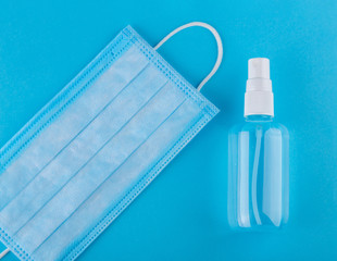 Medical face mask and sanitizer on blue, top view. Top view of disposable medical surgical protective face mask with antibacterial antiseptic bottle on blue background. Protection against coronavirus.