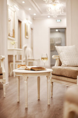 An open vintage book, a glass of white wine and crunchy pastries sit on a vintage table in the bright, cozy living room