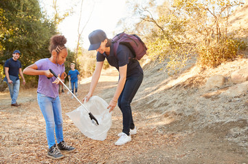 Adult Team Leader With Group Of Children At Outdoor Activity Camp Collecting Litter Together