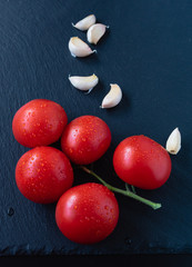 Branch of ripe red tomatoes and chives on a black background. Fresh ingredients for the salad.