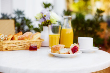 Fresh pastries, coffee, jam, a decanter and a glass of orange juice stand on a table decorated with a bouquet of delicate flowers on the terrace. Romantic Breakfast in the fresh air