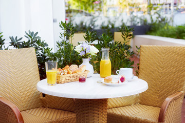 Fresh pastries, coffee, jam, a decanter and a glass of orange juice stand on a table decorated with a bouquet of delicate flowers on the terrace. Romantic Breakfast in the fresh air