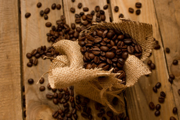 Wypalone ziarna czarnej kawy, rozsypujące się z worka jutowego na surowe deski. © trojan74