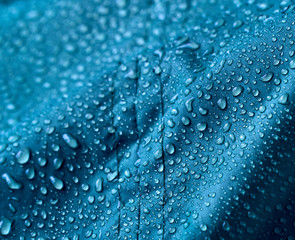 Rain water droplets on blue fiber waterproof fabric. Blue background.