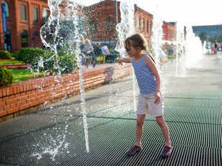 Little amused girl in sunglasses playing by the streams of the city fountain in Manufaktura in Lodz...