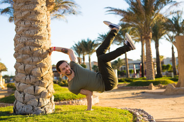 Athletic young handsome man,doing a handstand on summer holiday,relaxing in beach hotel resort with palms,b-boy outdoors,workout