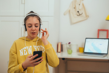 Fototapeta premium preteen girl sitting desk at her room using smartphone listening music