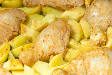 Chicken legs with potato slices are baked on a baking sheet from the oven close-up.