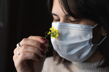 mujer oliendo una flor con un barbijo en cuarentena woman smelling a flower with a chin mask