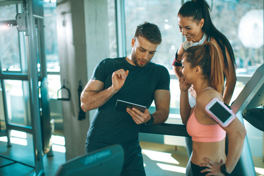 Personal trainer looking at digital tablet and explaining progress to young women at the gym