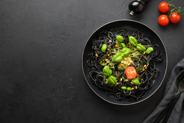 Black pasta spaghetti squid Ink with sauce Pesto in black bowl on black stone background. Top view.
