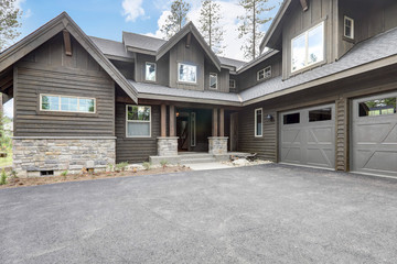Classic rustic new home in dark grey wood exterior with forest landscape with tall pine trees.