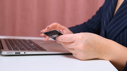 female hands make a purchase on the Internet using a laptop, payment by card, close-up.