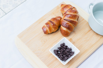 homemade whole spelled flour croissants, on a wooden surface, next to chocolate chips in a small ceramic square bowl,