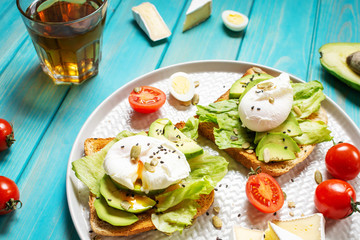 Healthy sandwich - poached eggs and avocado on toast with tomatoes on blue wooden background.