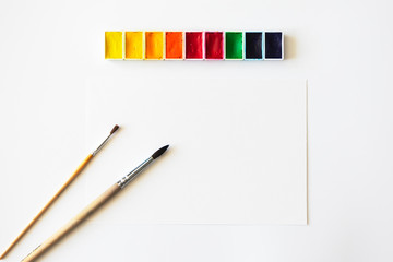 Blank empty paper sheet, paintbrushes and colorful watercolor on white background. Creative...